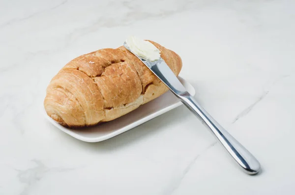 Croissant y un cuchillo con mantequilla en una mesa de piedra blanca. Francés — Foto de Stock