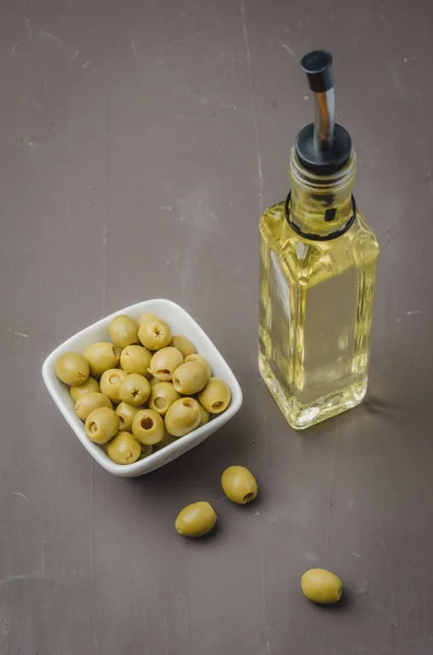 Glass bottle of olive oil and olive in a white bowl on a dark ba