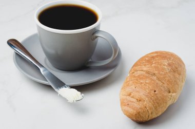 Kruvasanla kahve molası, tereyağı bıçağı ve bir fincan sade kahve.