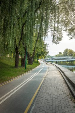Nehir boyunca yeşil ağaçlarla parktaki bisiklet yolu. Güzellik