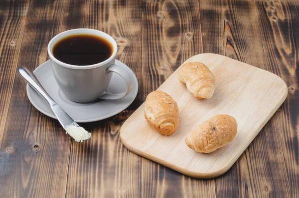 Xícara cinza com café preto e bandeja de madeira com croissants em wo — Fotografia de Stock