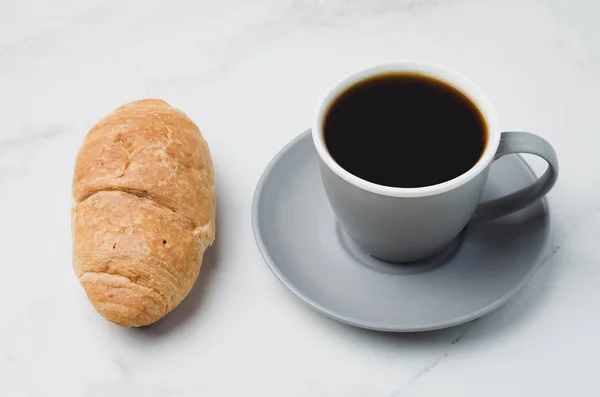 Перерыв на кофе. Серый стакан с черным кофе и круассан на белом — стоковое фото