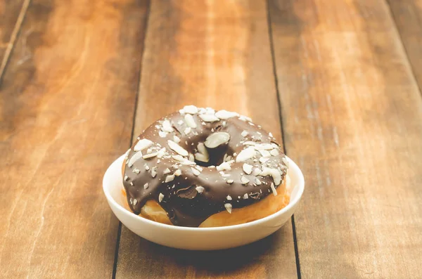 Donat in chocolate glaze is strewed with almonds. Wooden backgro — 图库照片