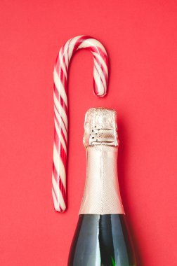 Kırmızı arka planda bir şişe şampanya ve baston şeker..