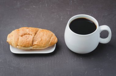 Siyah kahve ve kruvasan ile koyu taş masada beyaz kupa. C