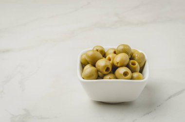 Beyaz arka planda beyaz bir seramik kasede yeşil zeytin. Anlaşıldı.