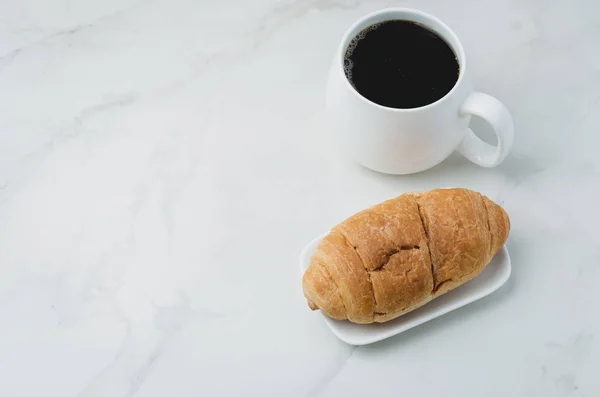 Taza blanca con café negro y croissant en mesa de piedra blanca . — Foto de Stock