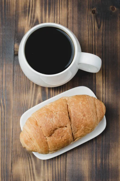 Taza blanca con café negro y croissant sobre fondo de madera . — Foto de Stock