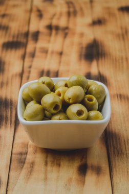 Ahşap zemin üzerinde beyaz bir seramik kasede yeşil zeytin. Oli.