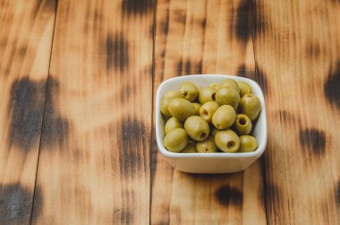 Ahşap zemin üzerinde beyaz bir seramik kasede yeşil zeytinler