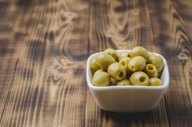 Ahşap zemin üzerinde beyaz bir seramik kasede yeşil zeytinler