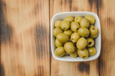 Ahşap zemin üzerinde beyaz bir seramik kasede yeşil zeytin. Üst