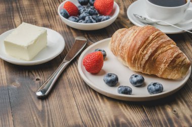 Kahve fincanı, kruvasan, beyaz kasede böğürtlen ve tereyağı.