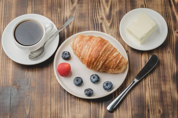 Taza de café, croissant con bayas en tazón blanco y cuchillo de mantequilla — Foto de Stock