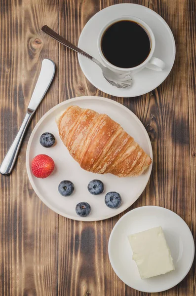 Xícara de café, croissant com bagas em tigela branca e faca de manteiga — Fotografia de Stock