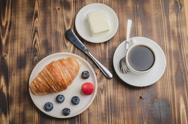 Coffee cup, croissant with berries in white bowl and butter knif