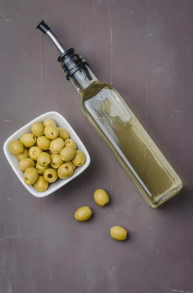 Bottiglia di vetro di olio d'oliva e oliva in una ciotola bianca su una ba scura — Foto Stock
