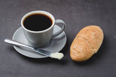 Kruvasanla kahve molası, tereyağı bıçağı ve bir fincan sade kahve.