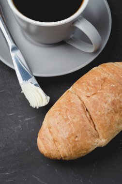 Kruvasanla kahve molası, tereyağı bıçağı ve bir fincan sade kahve.