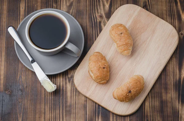 Taza gris con café negro y bandeja de madera con croissants en wo — Foto de Stock