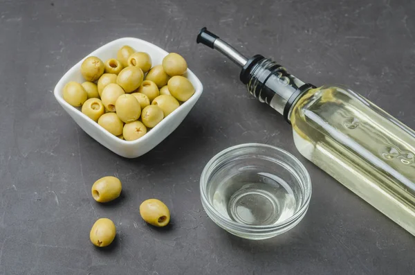 Bottiglia di vetro di olio d'oliva e oliva in una ciotola bianca su una ba scura — Foto Stock