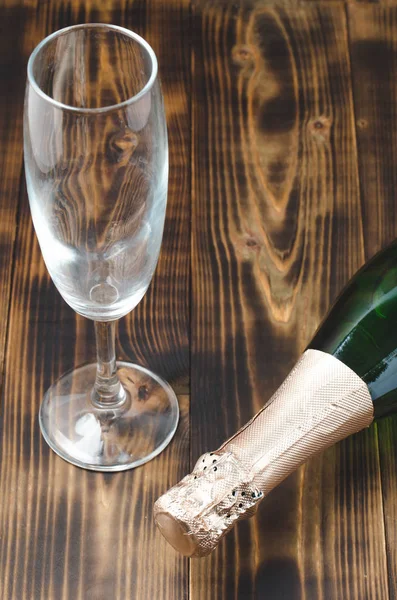 Bottle of sparkling wine and a glass on a wooden background. Top