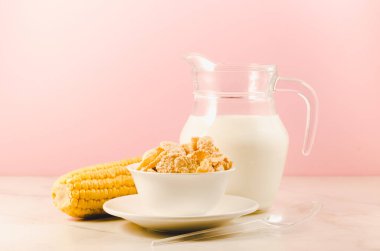 Mısır gevreği ve süt / mısır gevreği ile süt ve pembe arka planda bir mısır kulağı.