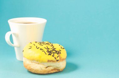 Mavi arka planda donut ve kahve fincanı koyu çikolata çubukları ve izole edilmiş kahve fincanı ile süslenmiş sarı jöleli donut. Boşluğu kopyala