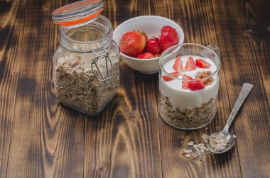Sağlıklı kahvaltı. Yoğurt, taze çilek, ahşap bir masada açık cam kavanozda ev yapımı granola..