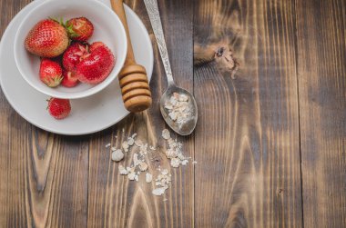 Beyaz bir kasede çilek, tatlım ve tahta bir arka planda kaşıkta granül. Üst görünüm, alanı kopyala