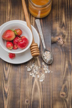 Beyaz bir kasede çilek, tatlım ve tahta bir arka planda kaşıkta granül. Üst görünüm, alanı kopyala