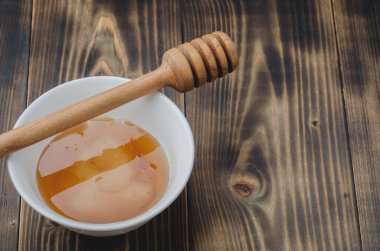 Beyaz bir kasede ballı, ahşap bir masa. Üst görünüm