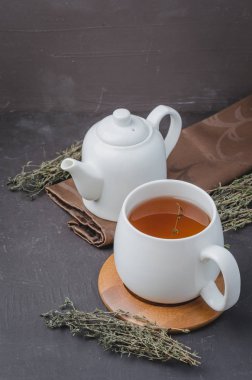 Beyaz fincanda kekik çayı ve siyah masada çaydanlık.. 