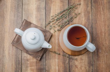 Kekikli bitki çayı, yüksek açıdan beyaz bardakta çay ve ahşap masada çaydanlık.