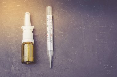 Drug spray bottle and thermometer on black background/Drug spray bottle and thermometer are placed on a black background. Copy space and top view
