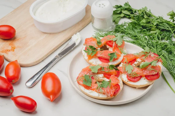 Healthy breakfast with round toast, red fish, vegetables and cheese/cooking of a breakfast with round toast with cheese, red fish, tomatoes and vegetables on a white table.