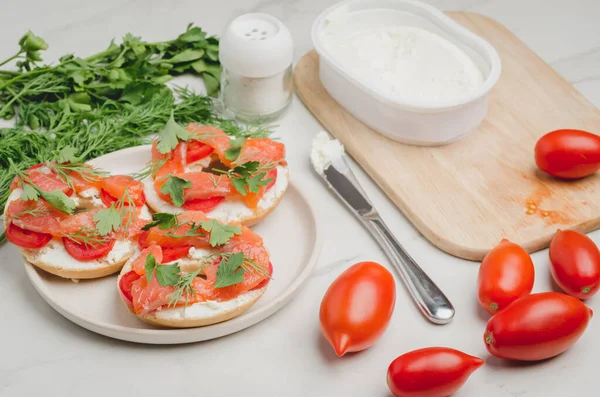 Healthy breakfast with round toast, red fish, vegetables and cheese/cooking of a breakfast with round toast with cheese, red fish, tomatoes and vegetables on a white table.