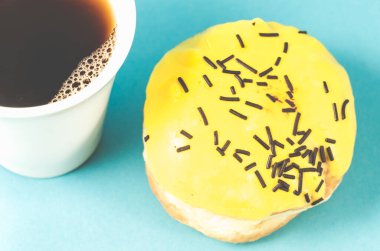 Mavi arka planda donut ve kahve fincanı koyu çikolata çubukları ve izole edilmiş kahve fincanı ile süslenmiş sarı jöleli donut. Kapat.