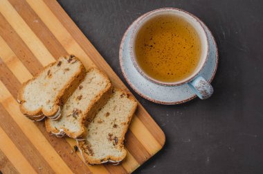 Çay fincanı ve hamur işleriyle kahvaltı. Koyu taştan bir masada tahta tahtada dilimlenmiş. Üst görünüm