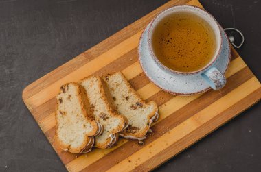 Çay fincanı ve hamur işleriyle kahvaltı. Koyu taştan bir masada tahta tahtada dilimlenmiş. Üst görünüm