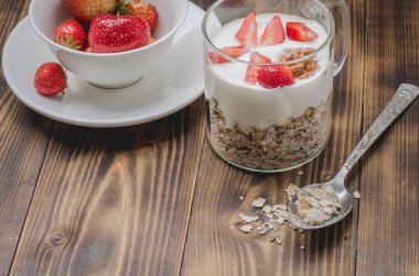 Sağlıklı kahvaltı. Yoğurt, taze çilek, ahşap bir masada dağınık granülle kaşık. Kopyalama alanı
