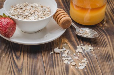 Tahta bir masada, beyaz bir kase içinde granül, bal kabı ve çilek hazırlamak..