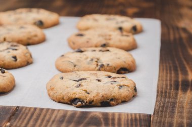 Kabartma kağıdı ve ahşap masa üzerinde çikolatalı kurabiyeler. Kabartma kağıdı ve ahşap masa üzerinde çikolatalı kurabiyeler. Taze hamur işleri.