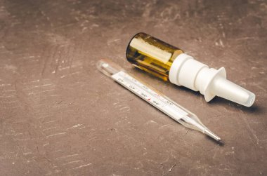 Drug spray bottle and thermometer on black background/Drug spray bottle and thermometer are placed on a black background. Copy space.