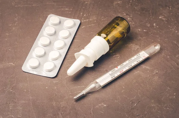 Drug spray bottle, pills packages and thermometer on black background/Drug spray bottle, pills packages and thermometer. Medicine subject. Top view.