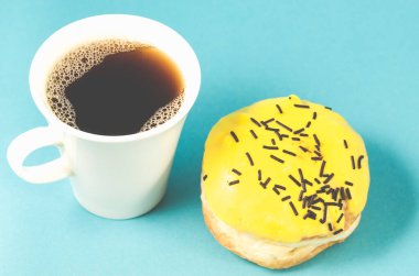 donut ve kahve fincanı mavi arka planda izole edilmiş / sarı jöleli donut ve mavi arka planda beyaz kahve fincanı. Üst görünüm