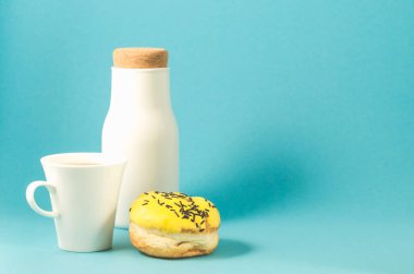 Sarı jöleli çörek, mavi arka planda kahve fincanı ve şişe. Koyu çikolata çubukları, mavi arka planda kahve fincanı ve şişe ile süslenmiş sarı jöleli donut. Boşluğu kopyala