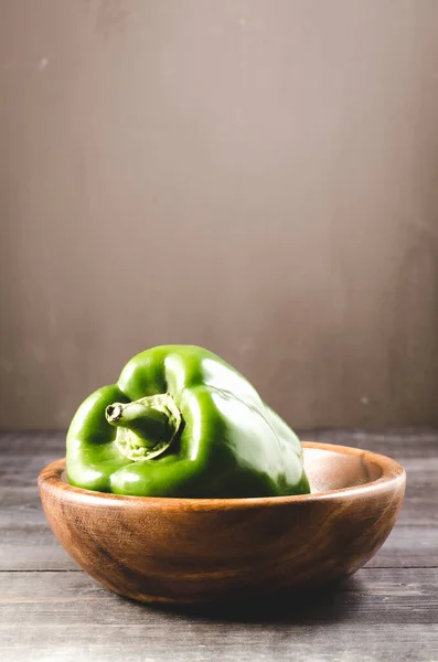 Green paprika on a wooden bowl/Green paprika pepper on a wooden bowl over dark wooden  background. Copy space above