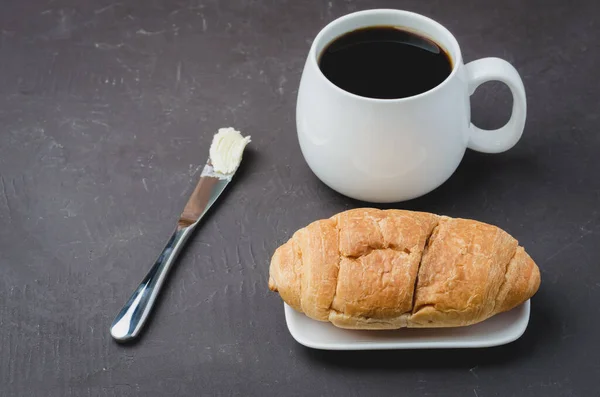 フランスの朝食 黒コーヒーとダークストーンテーブルのバターナイフでクロワッサンとホワイトマグカップ コーヒーブレイク — ストック写真