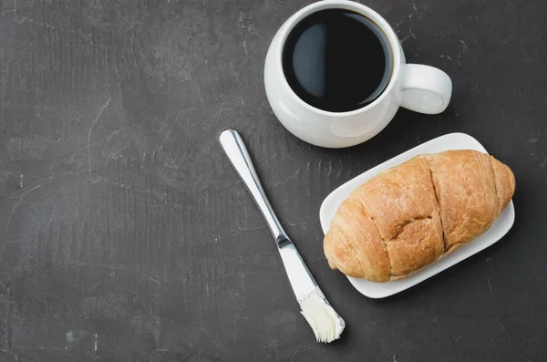 フランスの朝食 黒コーヒーとダークストーンテーブルのバターナイフでクロワッサンとホワイトマグカップ トップビュー コピースペース コーヒーブレイク — ストック写真